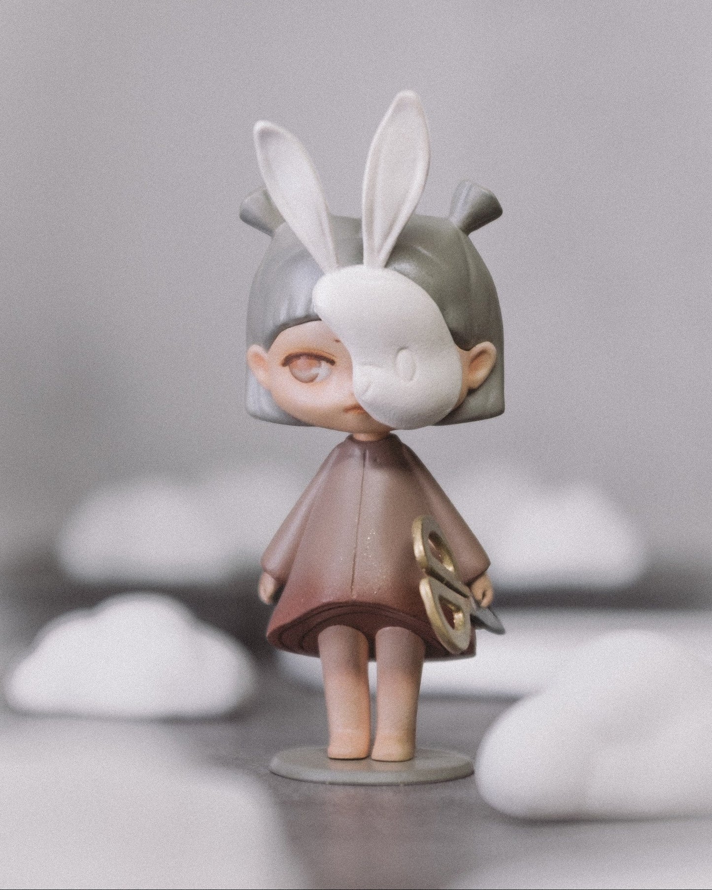 The Wanderer art toy, front view: a small hand-painted resin figure with white bunny ears, standing on a round base, holding gold scissors.