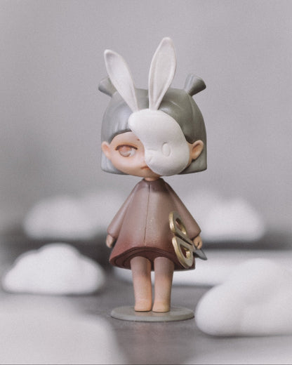 The Wanderer art toy, front view: a small hand-painted resin figure with white bunny ears, standing on a round base, holding gold scissors.