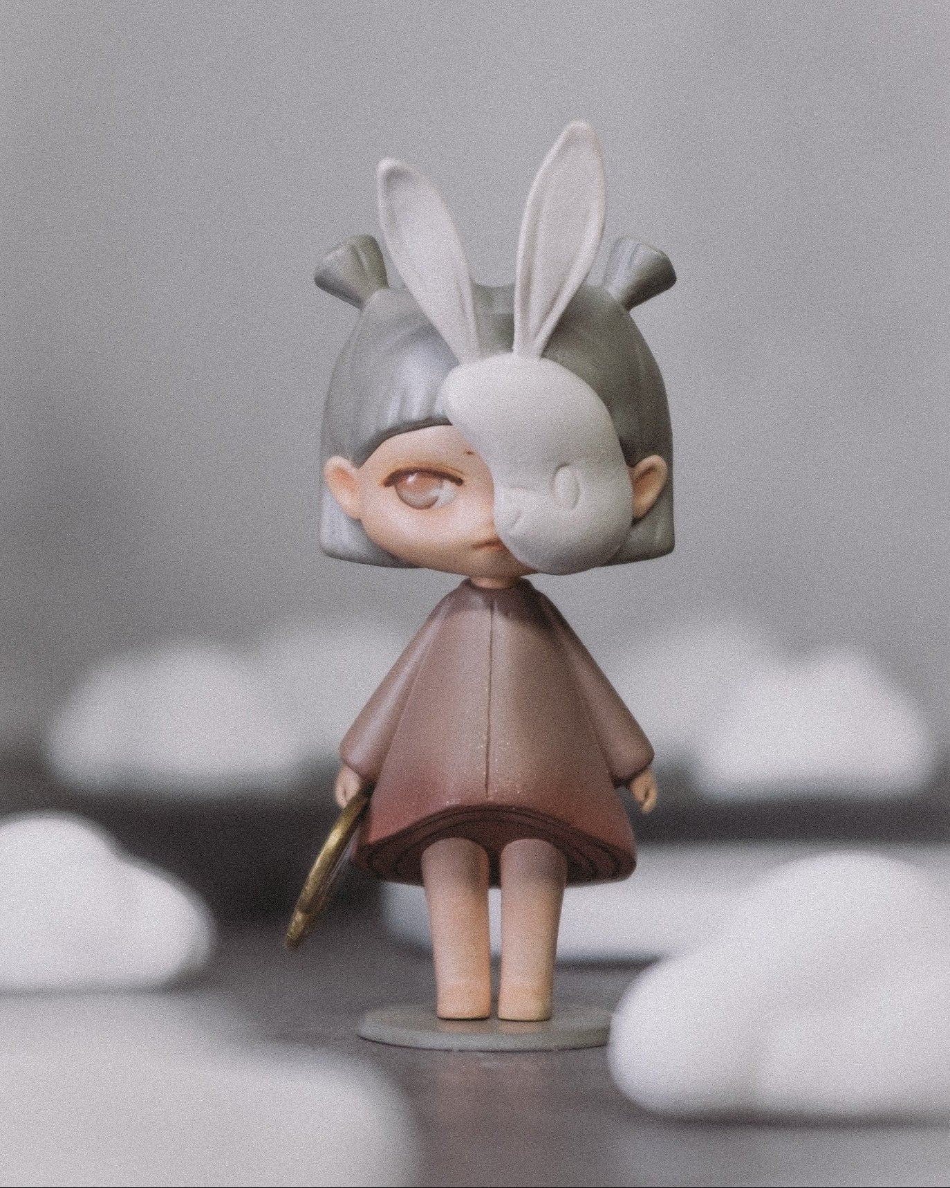 The Wanderer art toy standing against a soft grey background with cloud shapes behind her.