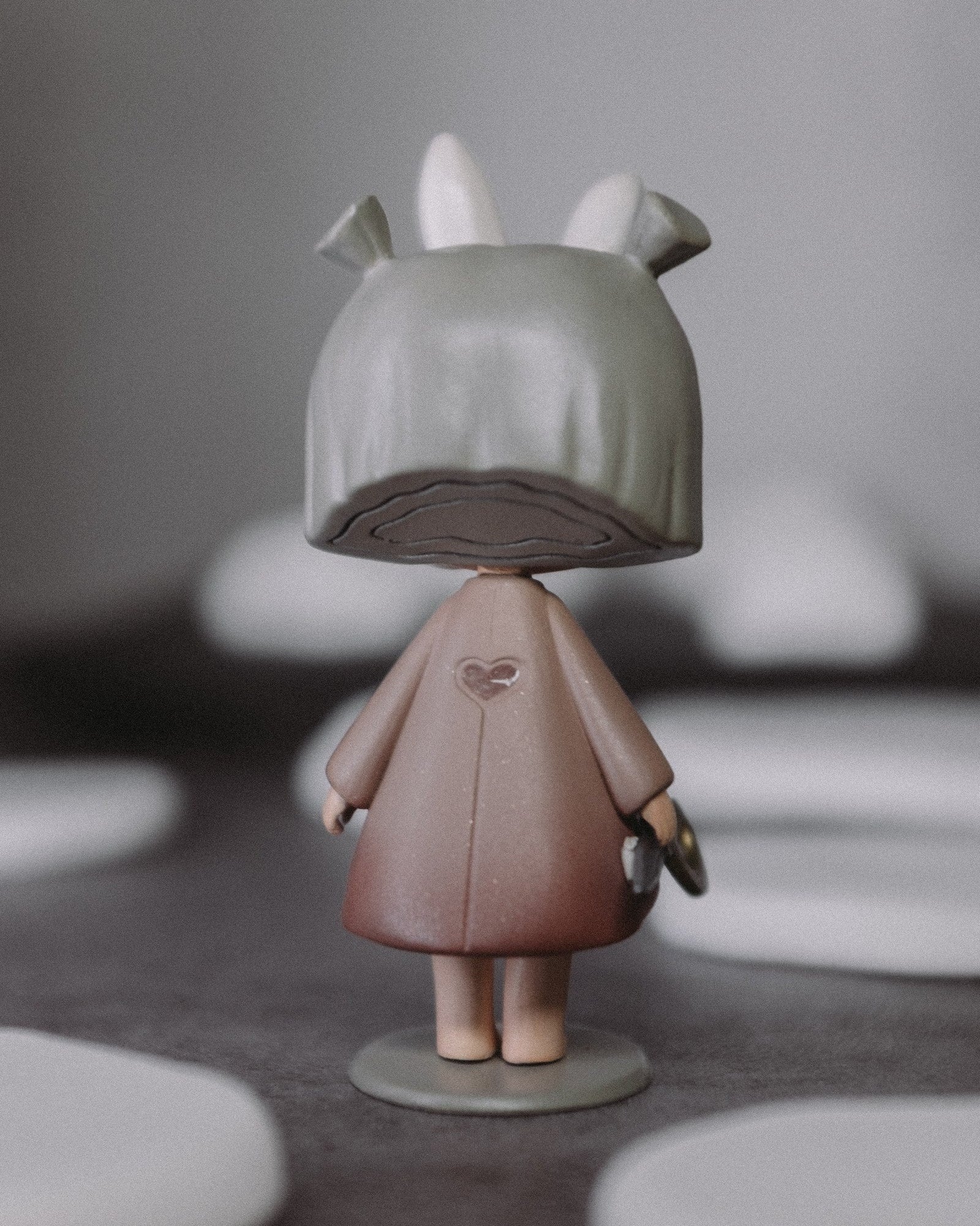 Back view of The Wanderer art toy, showing the hooded top with bunny ears and dusty pink coat.